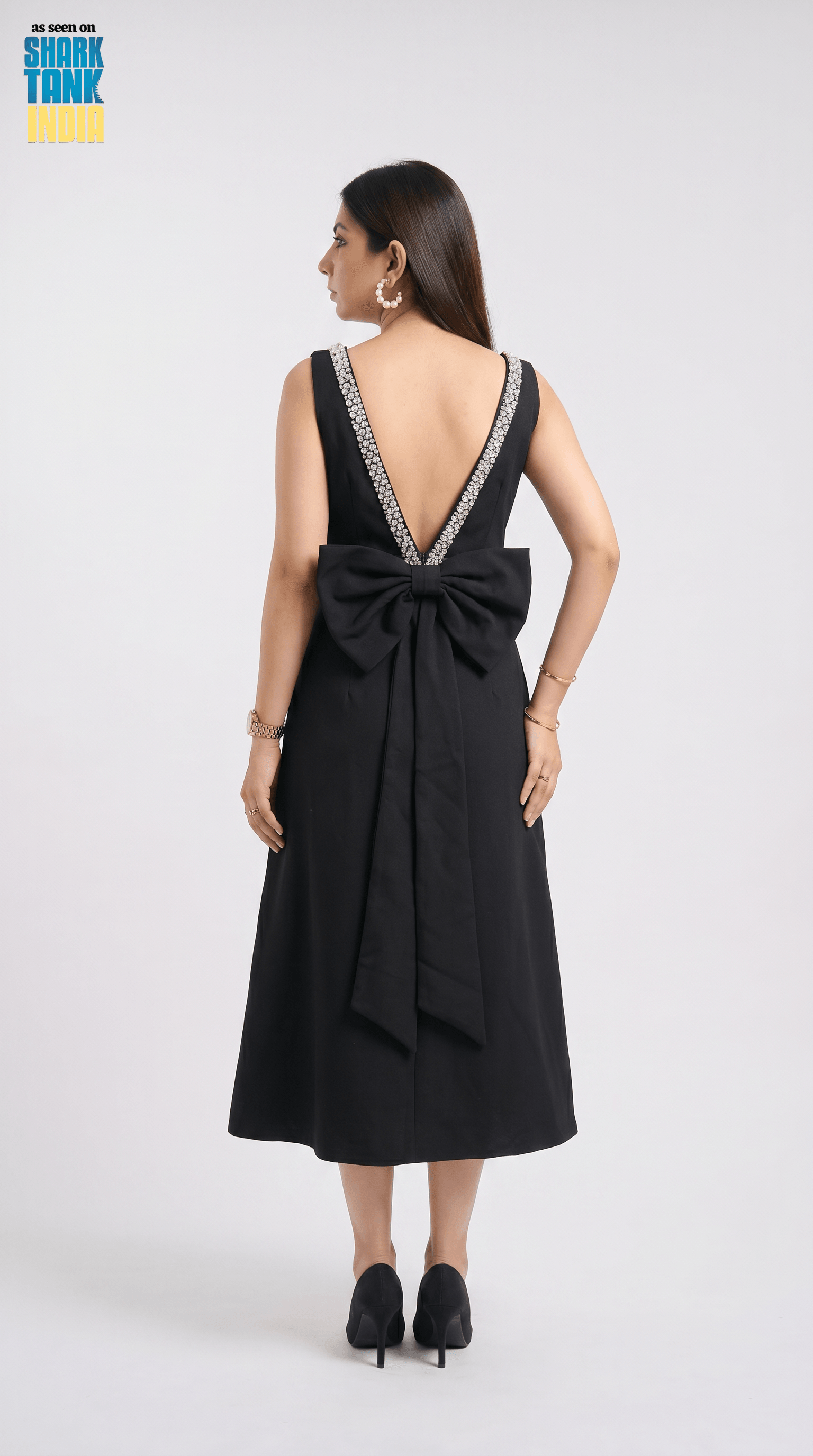 Black dress with a large bow detail on the back, worn by a model against a white background.