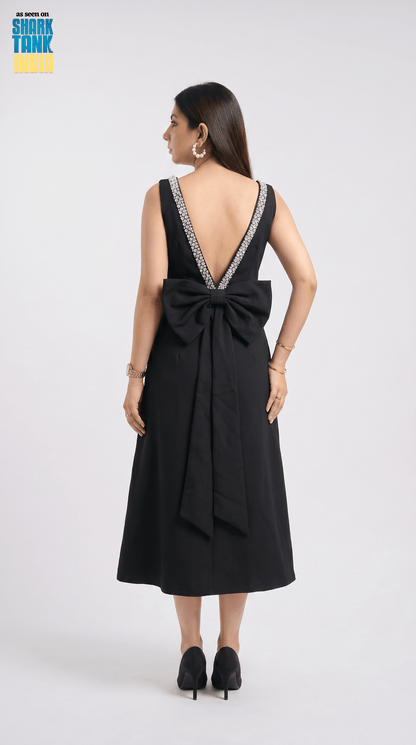 Black dress with a large bow detail on the back, worn by a model against a white background.