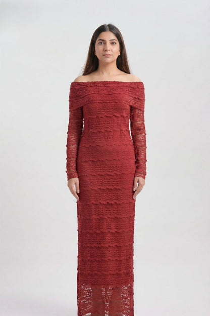 A woman modeling a long-sleeve off-the-shoulder maxi dress in textured red lace against a plain light gray studio background.