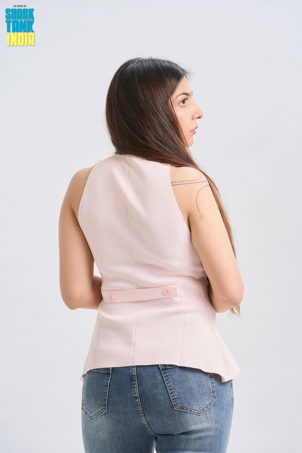 Woman wearing a light pink sleeveless top and blue jeans on a white background