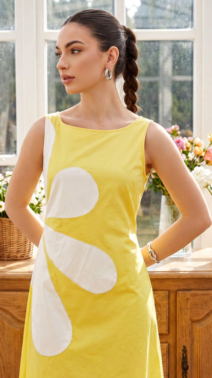 Woman wearing a yellow dress with a large white flower design in a sunlit room.