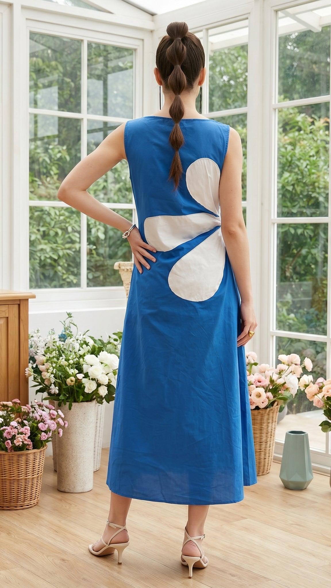 Woman wearing a blue dress with a white floral design in a bright room with large windows.