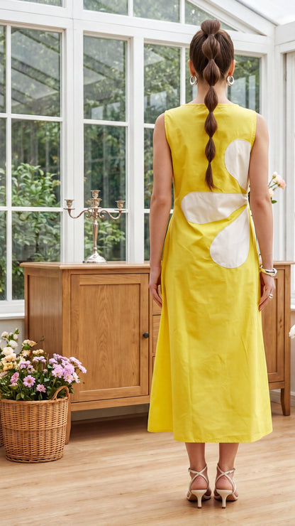 Woman in a yellow dress with a large white flower design standing in a sunroom.