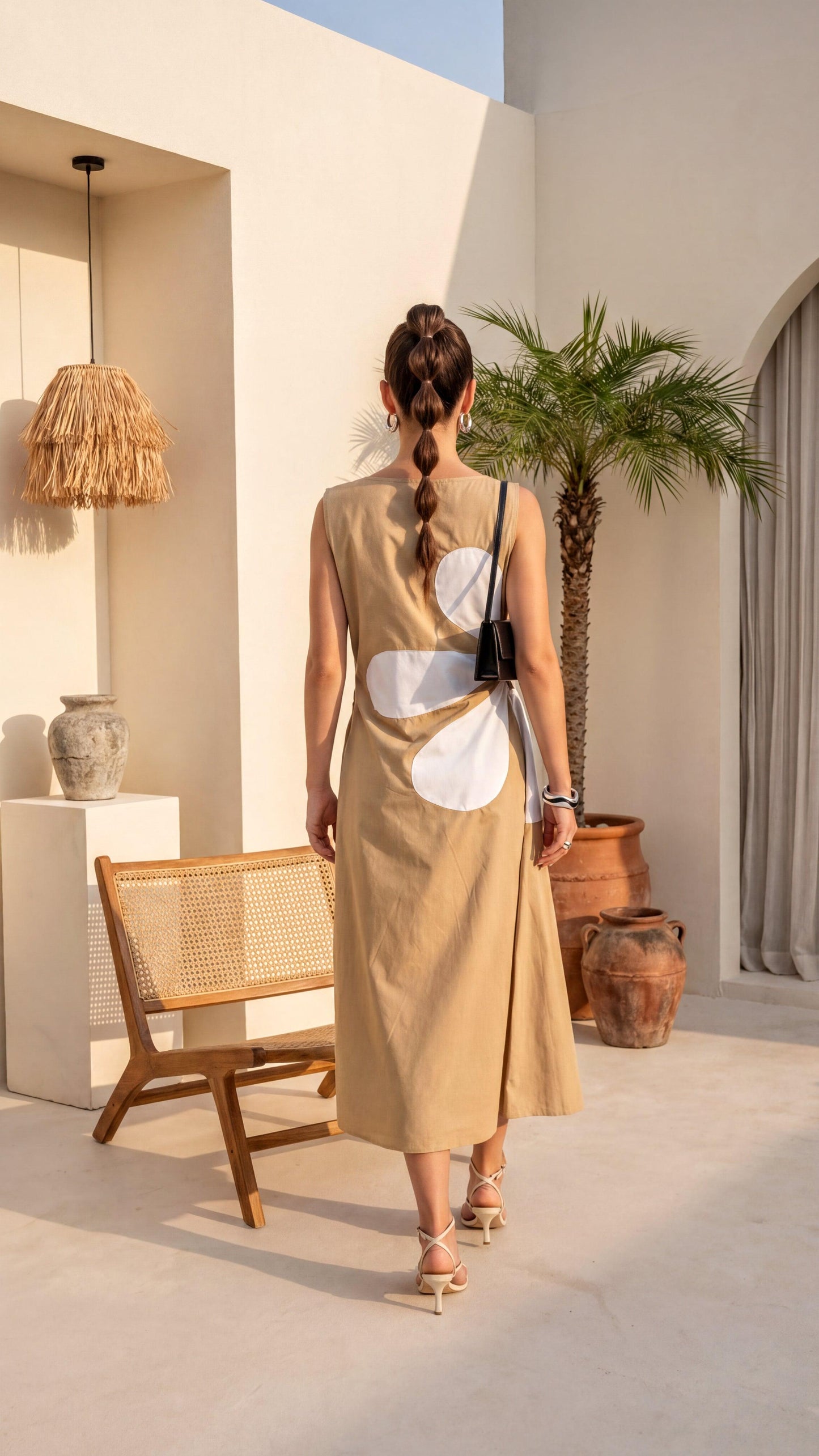 Woman in a beige dress standing in a sunlit outdoor setting with a chair and plants.