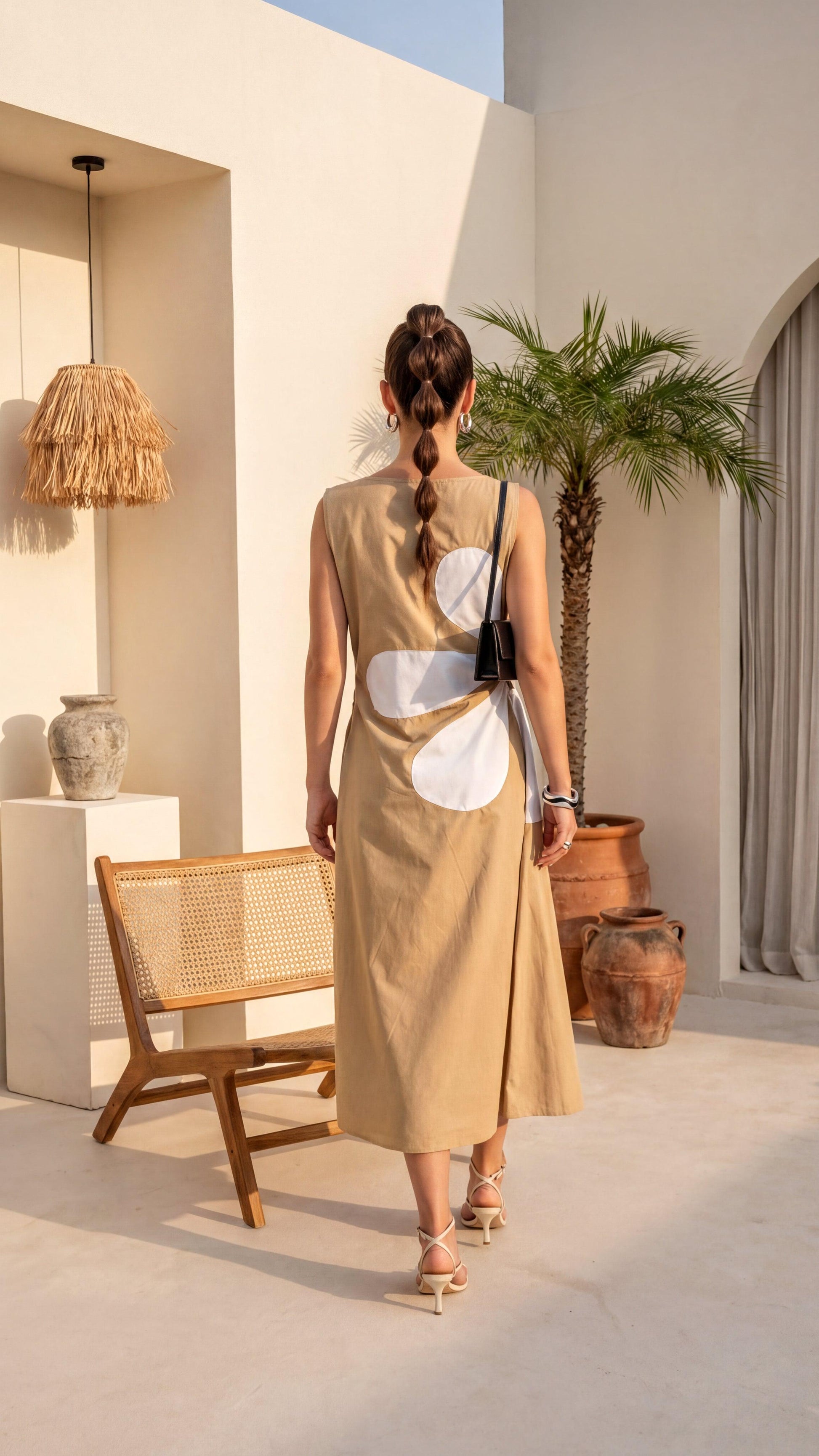 Woman in a beige dress standing in a sunlit outdoor setting with a chair and plants.
