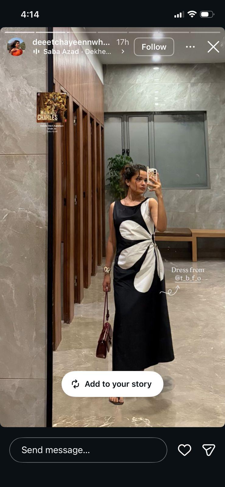 Woman taking a mirror selfie wearing a black dress with a white floral design in a bathroom.