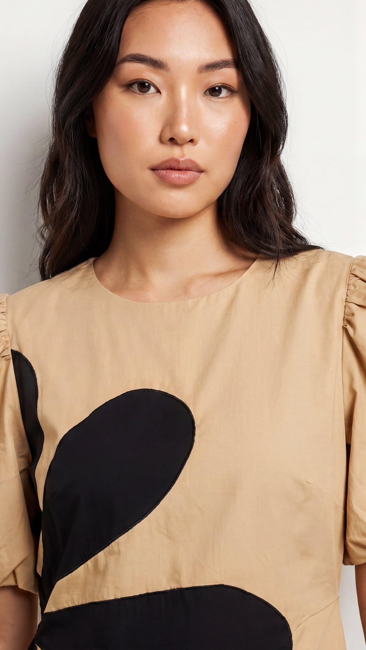 Woman wearing a beige top with black abstract shapes on a white background