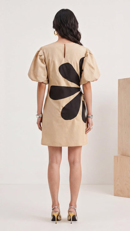 Woman wearing a beige dress with black floral design on the back against a white background