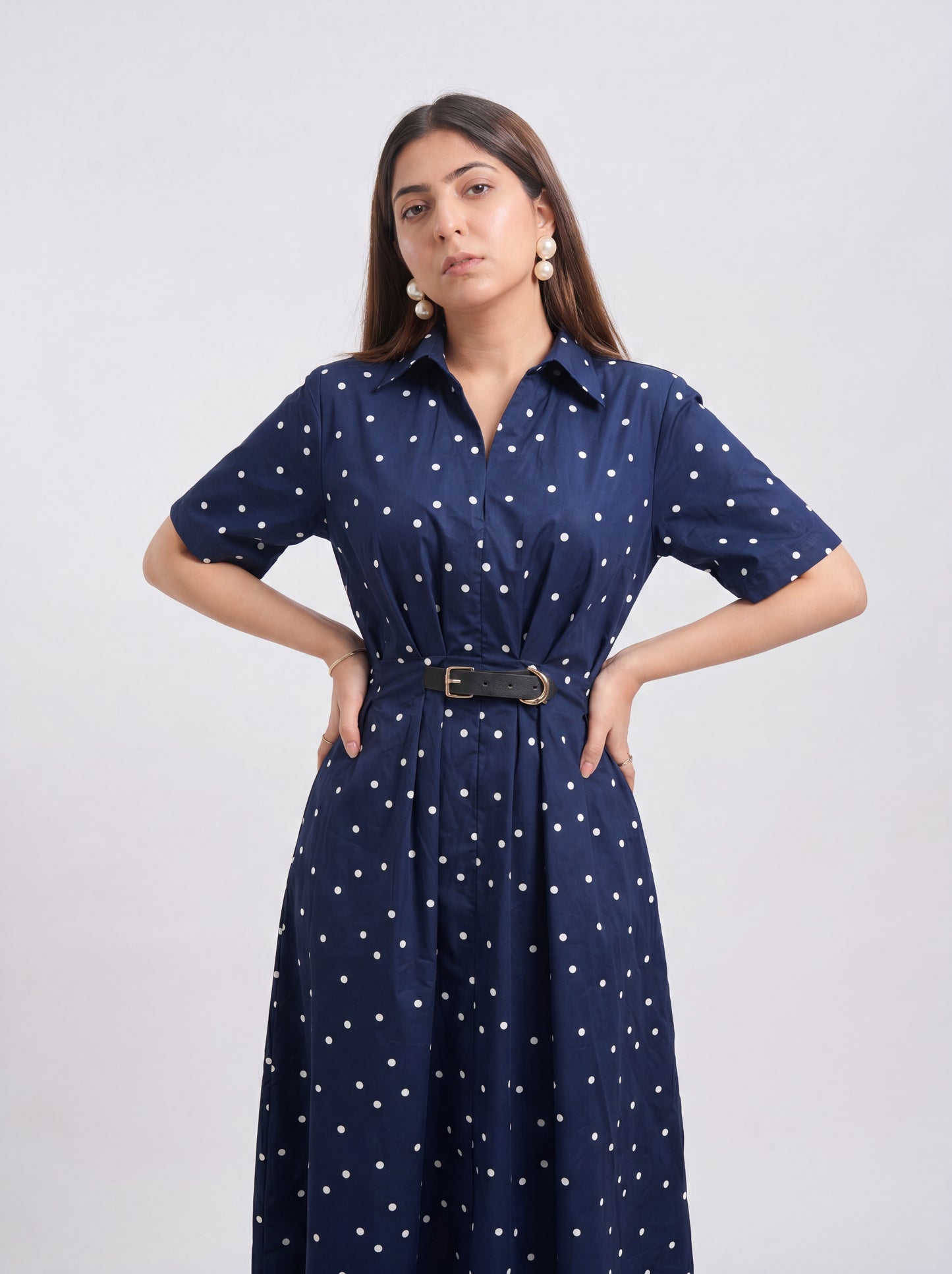 Woman wearing a navy blue dress with white polka dots on a light gray background
