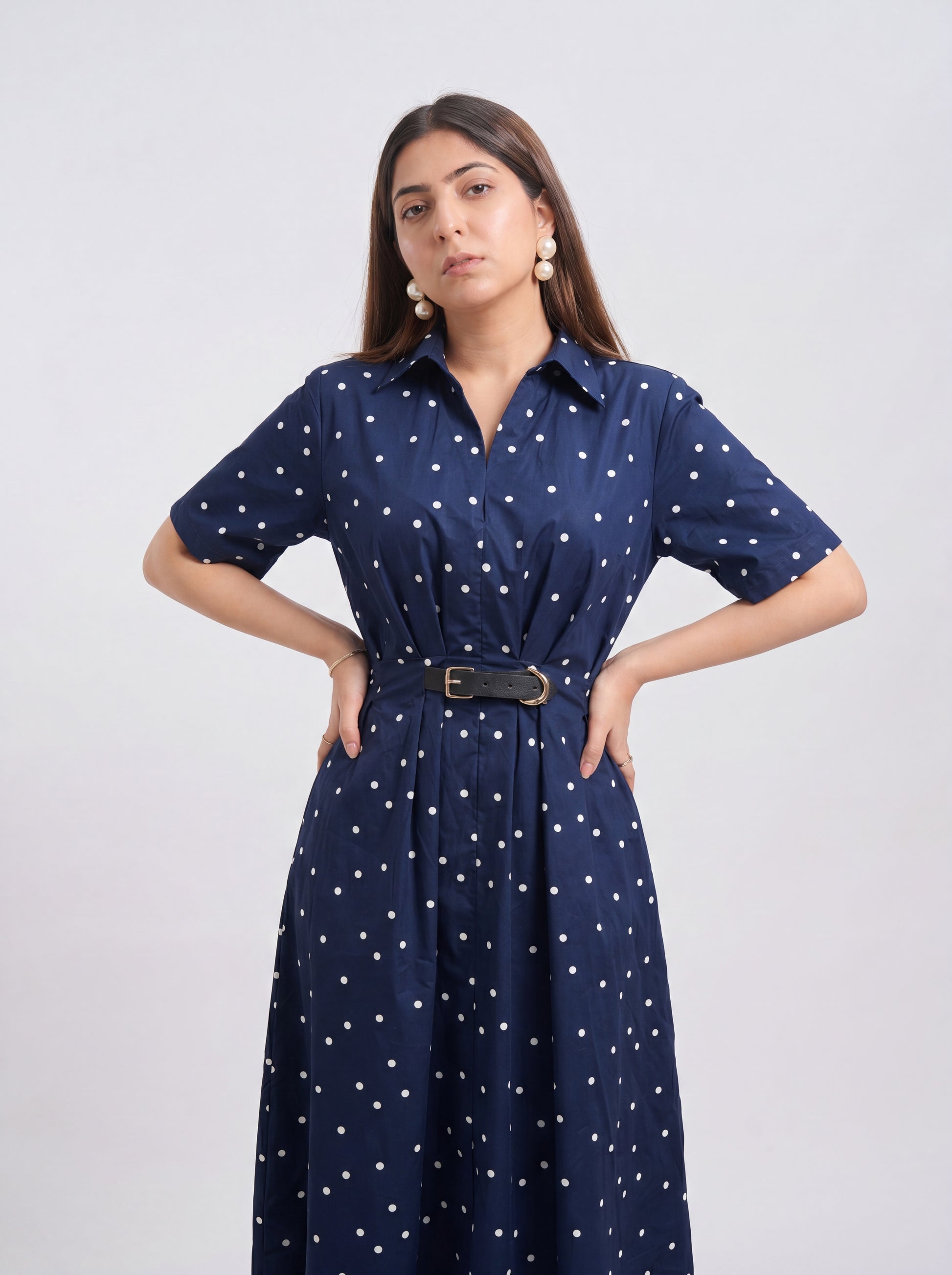 Woman wearing a navy blue dress with white polka dots on a light gray background