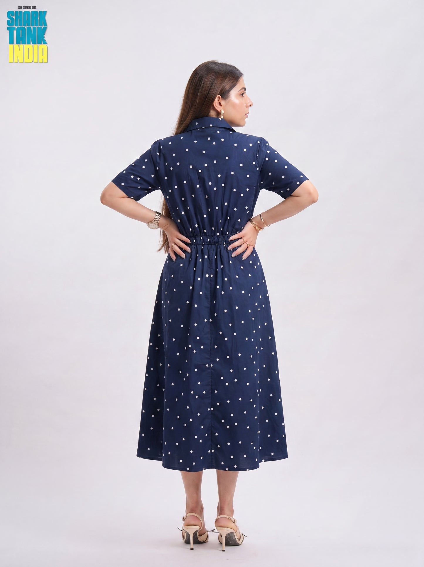 Woman wearing a navy blue dress with white polka dots on a light gray background