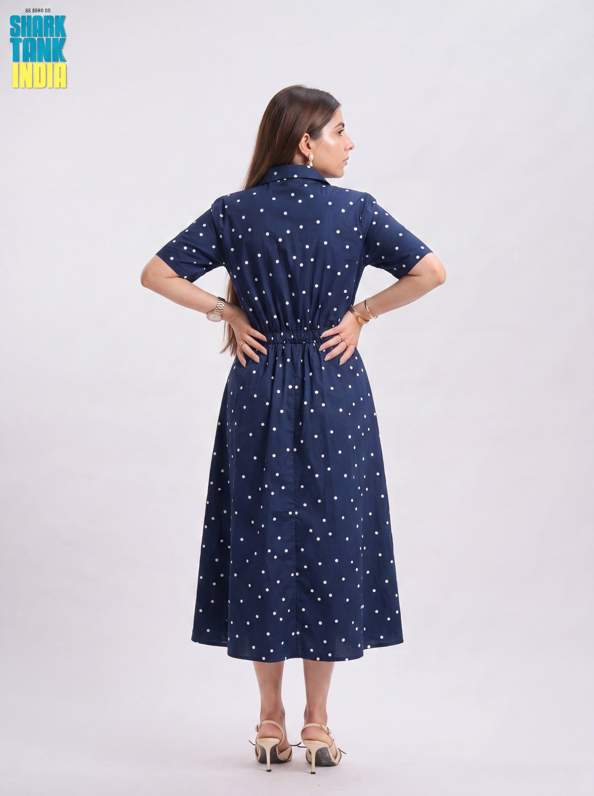 Woman wearing a navy blue dress with white polka dots on a light gray background