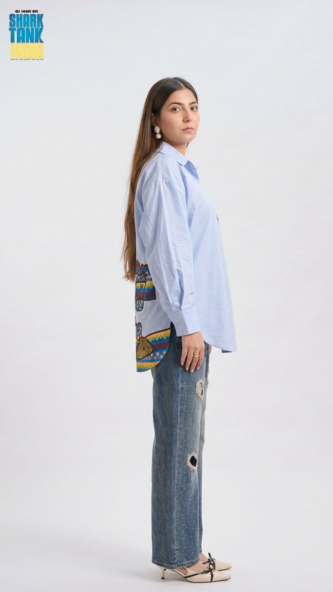 Woman wearing a light blue shirt and jeans with a colorful patterned bag on a white background