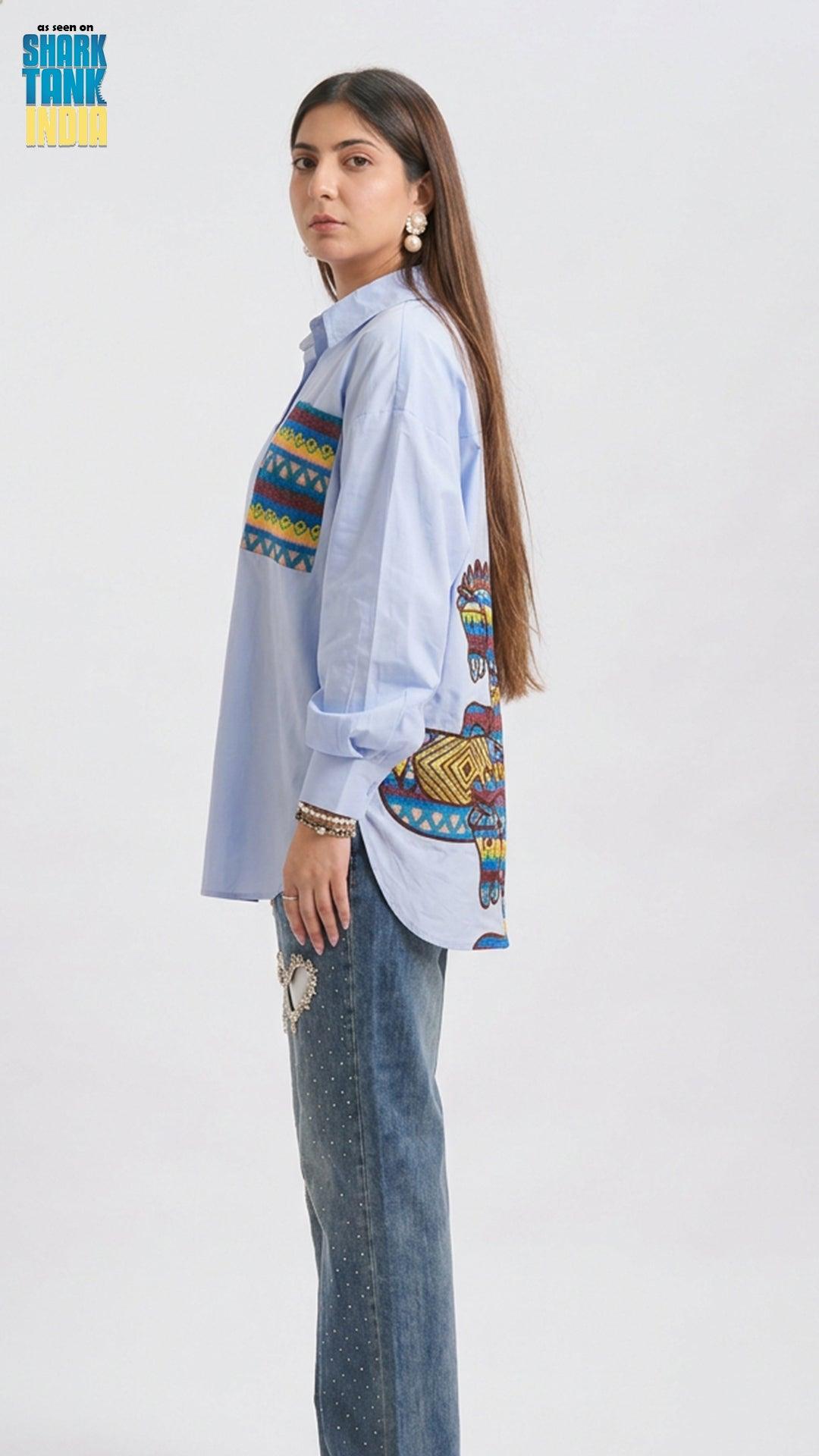 Woman wearing a light blue shirt with colorful patterns and jeans on a white background