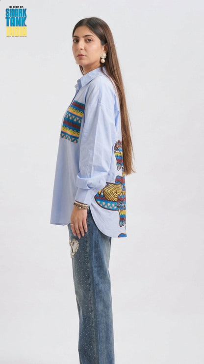Woman wearing a light blue shirt with colorful patterns and jeans on a white background