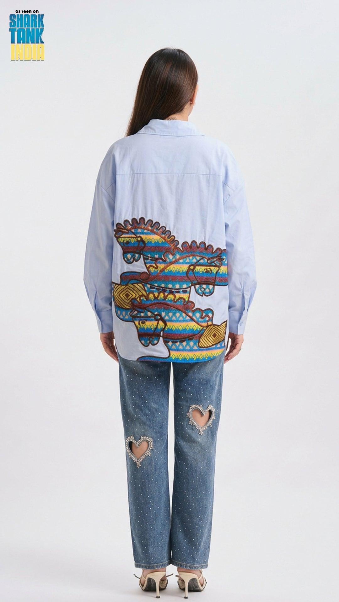 Person wearing a light blue denim jacket with a colorful graphic on the back, standing against a white background.