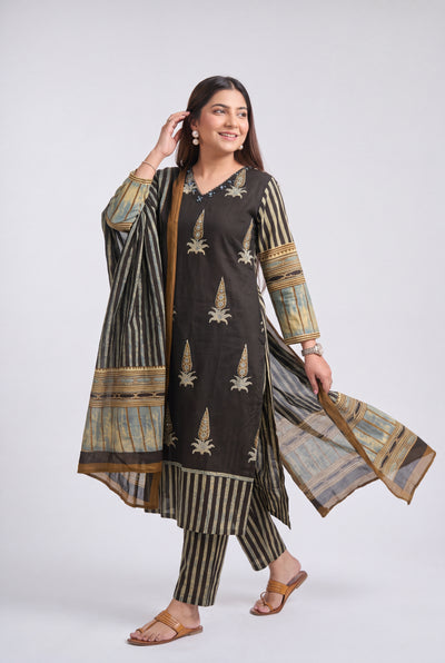 A woman modeling a traditional three-piece salwar kameez suit in dark brown and beige. The kurta features vertical beige stripes and embroidered motifs, paired with matching striped trousers and a sheer dupatta with beige and gold patterns, set against a plain light gray studio background.