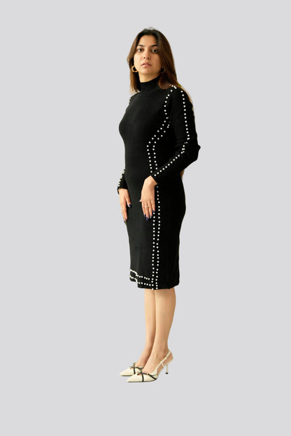 Woman wearing a black dress with white embellishments standing in front of a plant.