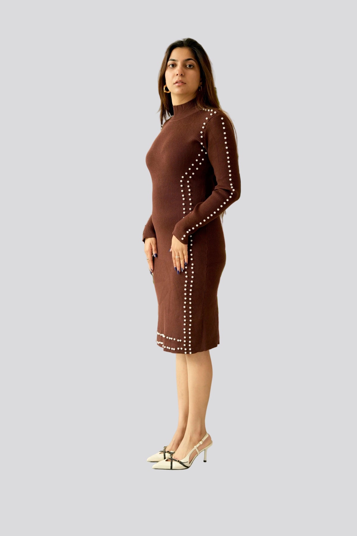 Woman wearing a brown dress with white embellishments standing in front of a plant.