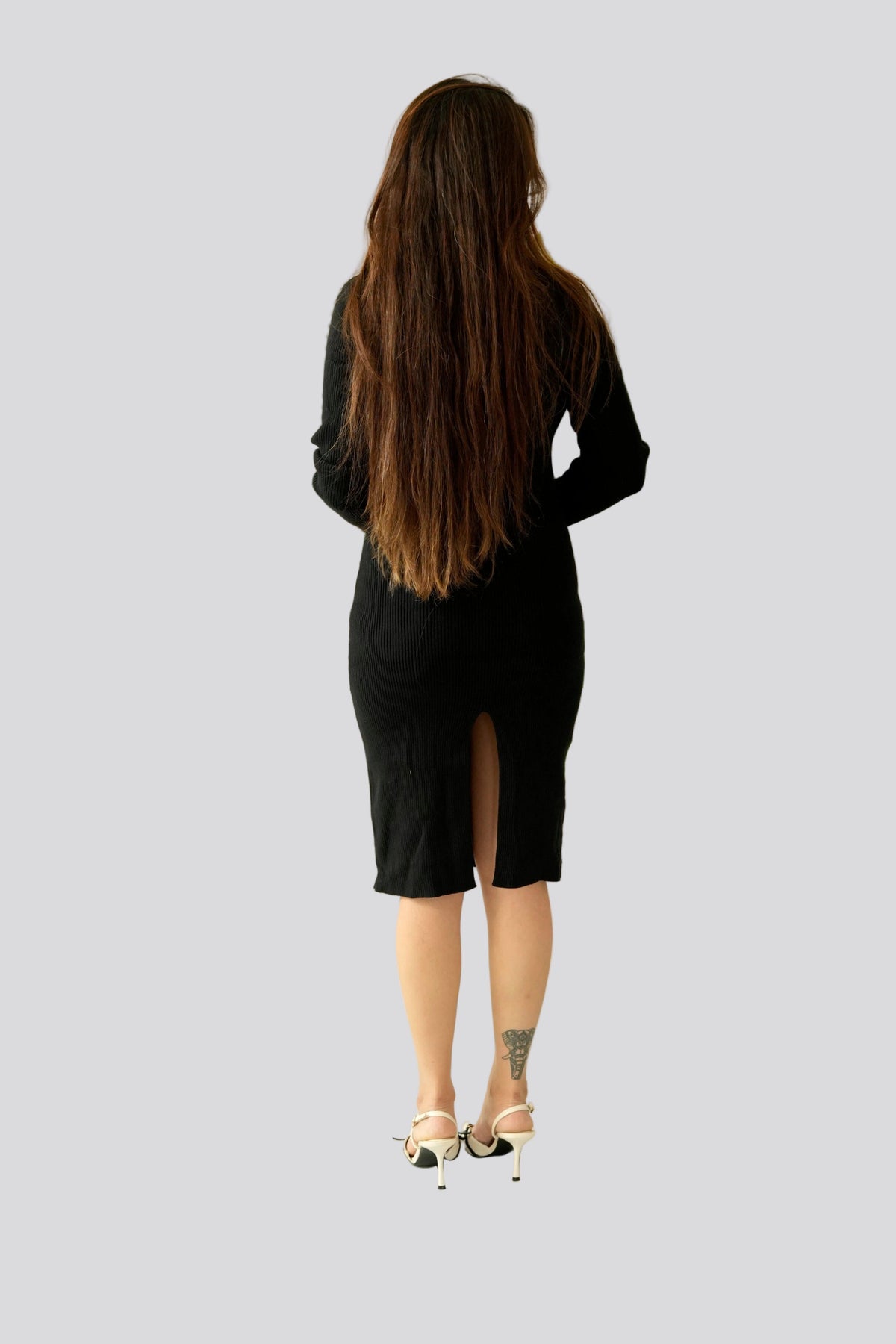 Woman in a black dress standing next to a large green plant against a white wall.