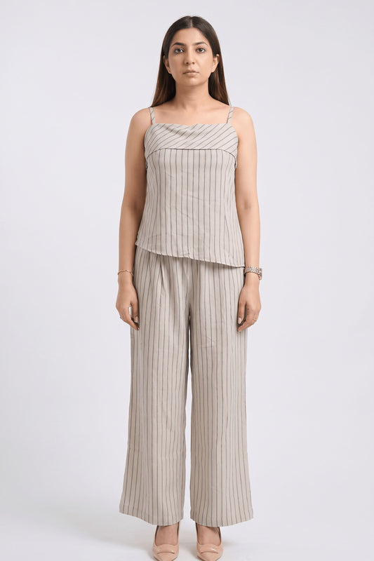 A woman modeling a matching two-piece set consisting of a sleeveless camisole top and wide-leg trousers, both in a light beige fabric with thin vertical gray stripes, shot against a plain light gray background.