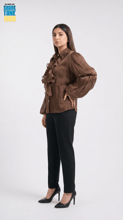 Woman wearing a brown blouse with ruffles and black pants on a white background