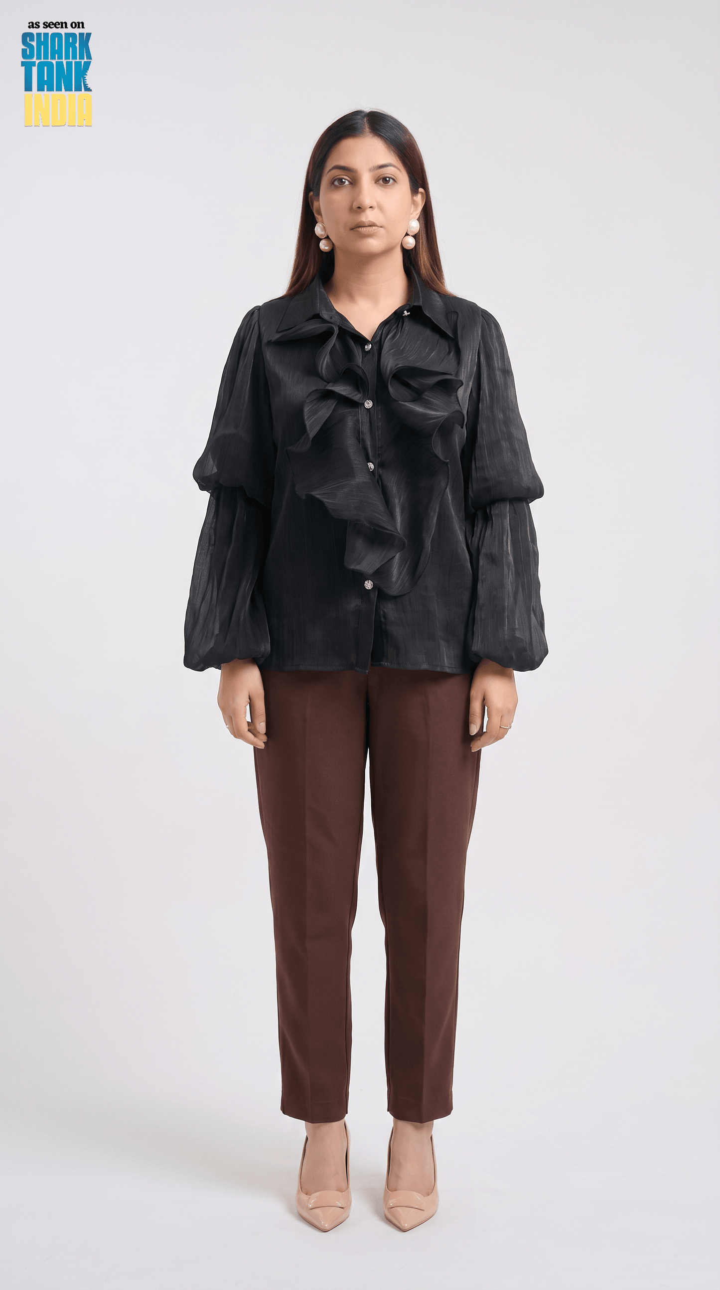 Woman wearing a black ruffled blouse and brown pants on a white background
