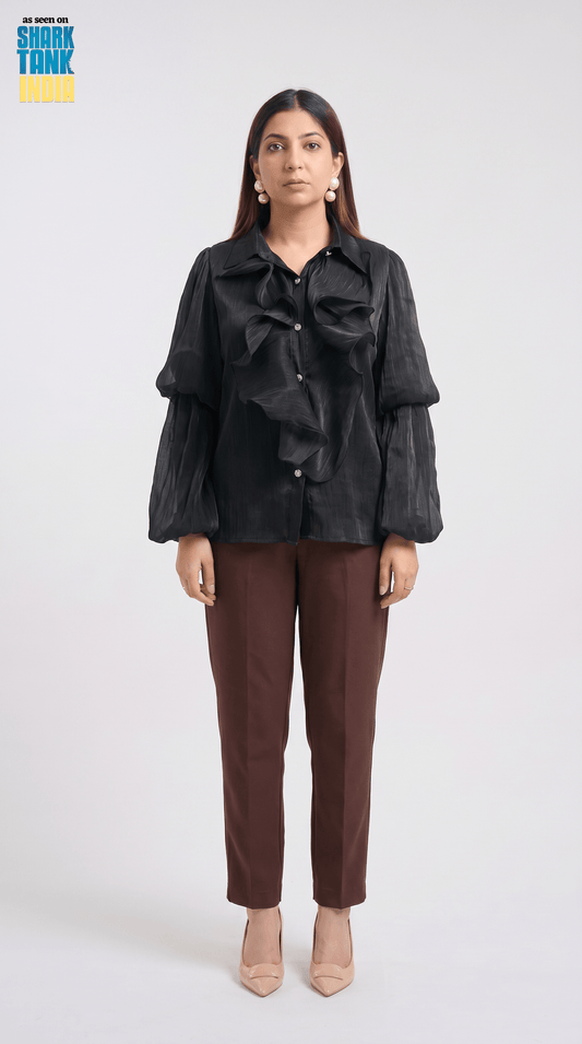 Woman wearing a black ruffled blouse and brown pants on a white background