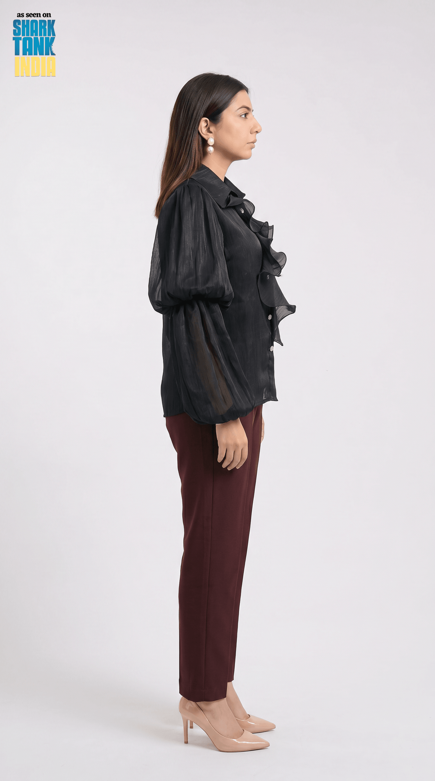 Woman wearing a black ruffled blouse and maroon pants on a white background