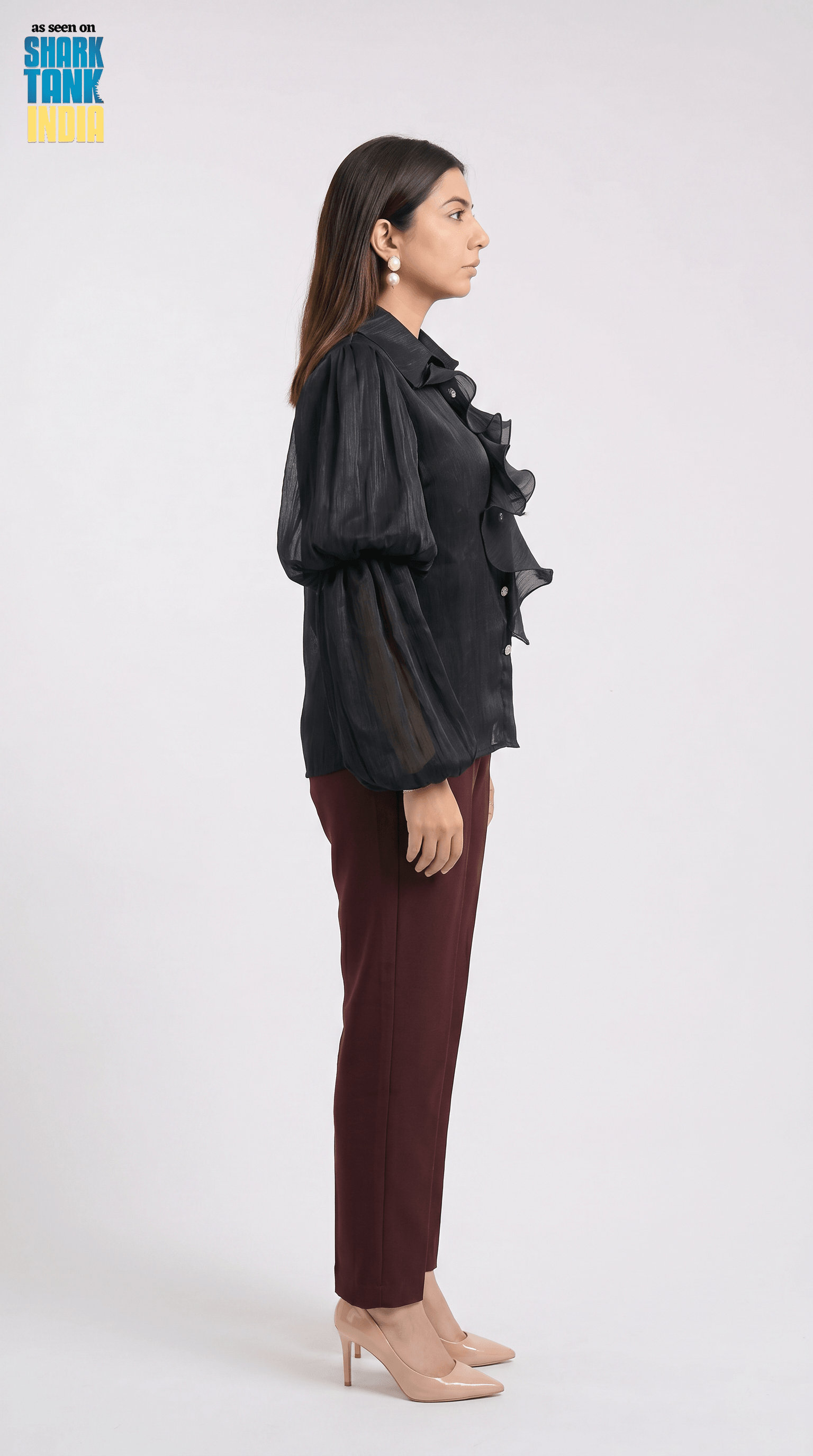 Woman wearing a black ruffled blouse and maroon pants on a white background