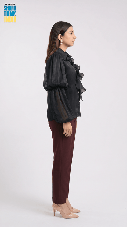 Woman wearing a black ruffled blouse and maroon pants on a white background