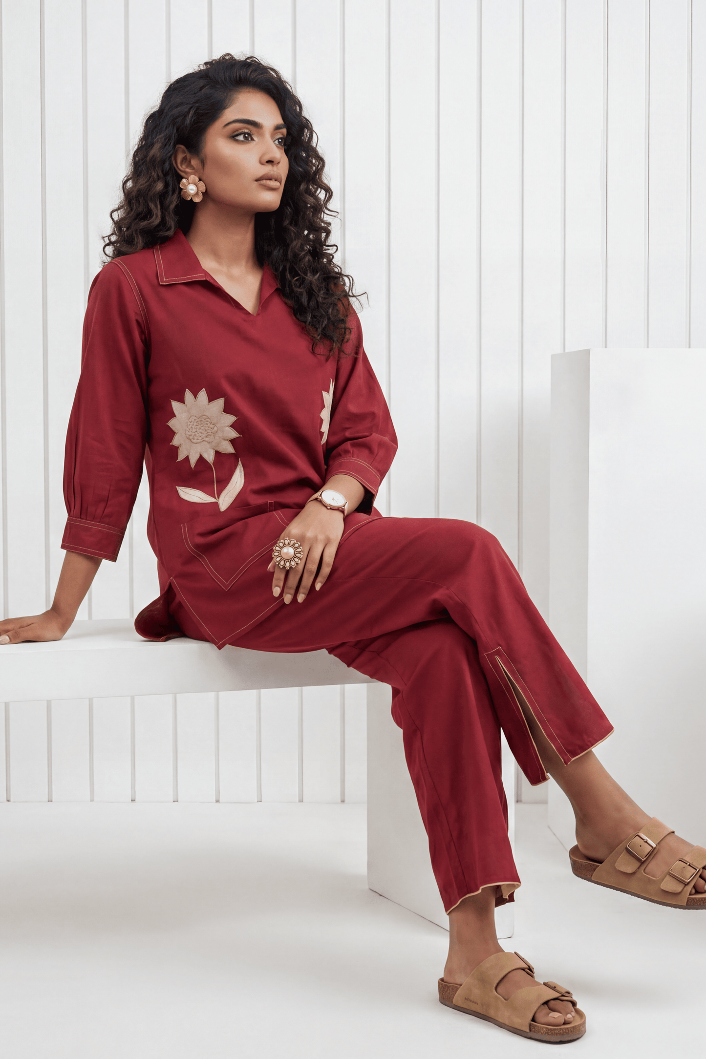 Woman wearing a red outfit with a sun design, sitting on a white bench.