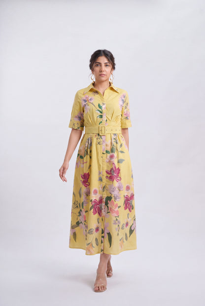 A woman modeling a yellow short-sleeve midi dress with a floral print, button-up front, and matching belt, photographed against a light gray studio background.