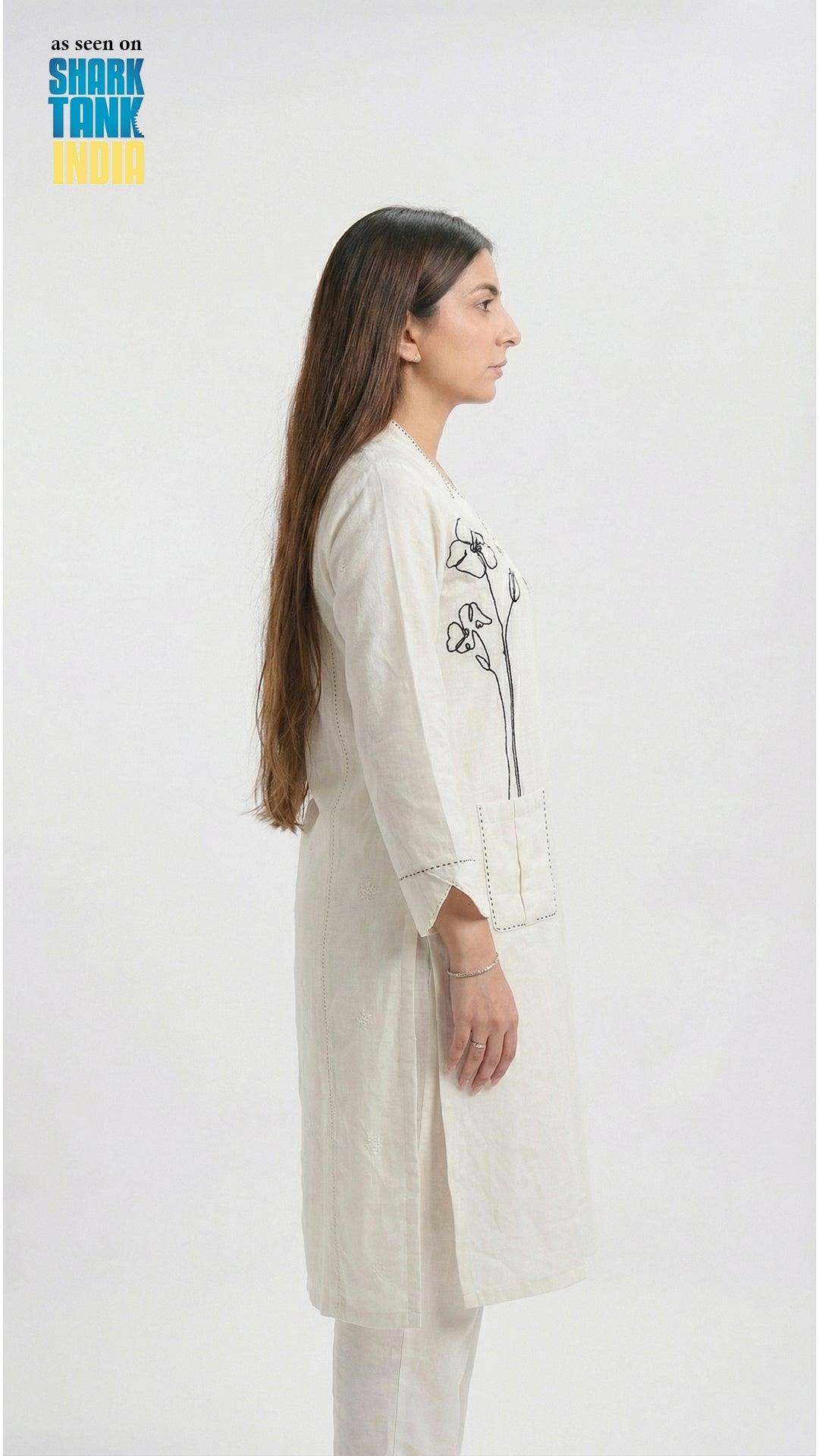 Woman wearing a white embroidered outfit on a plain background