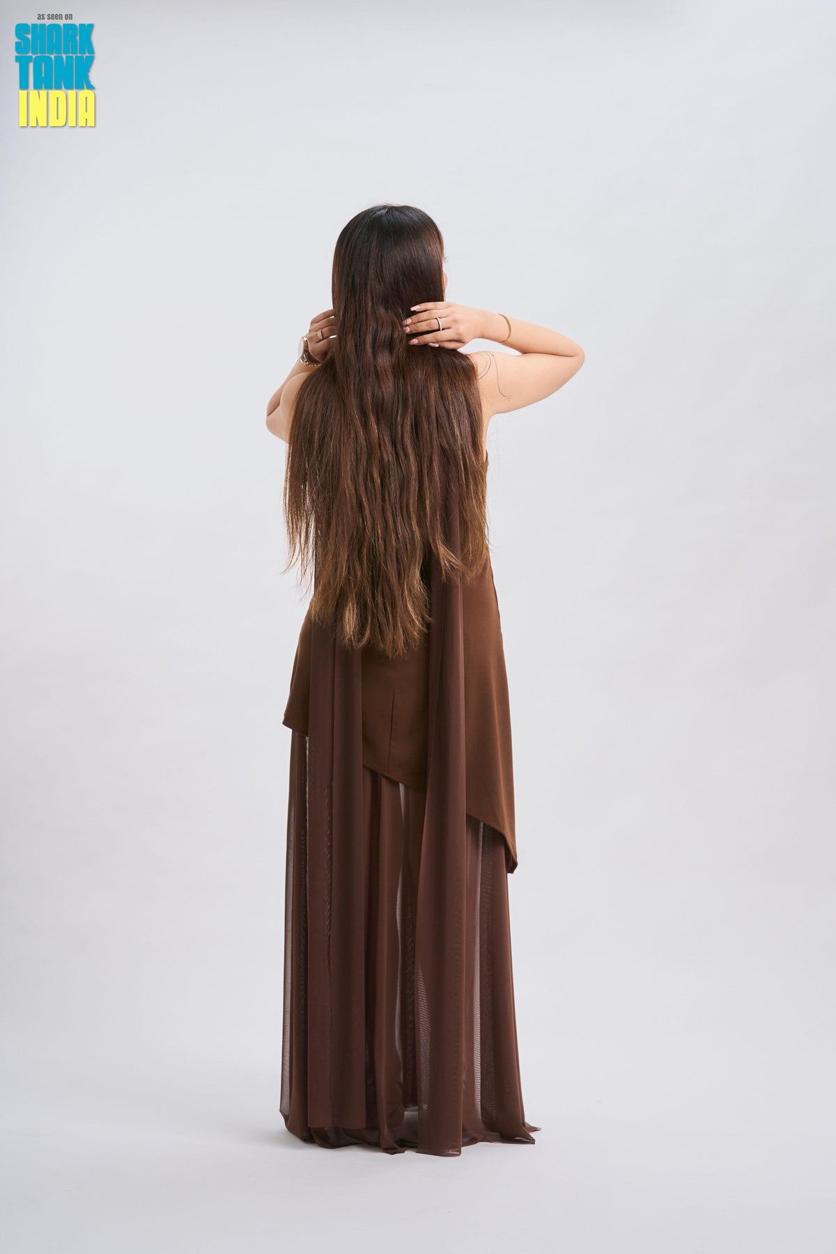 Woman in a brown dress with long hair, standing against a white background