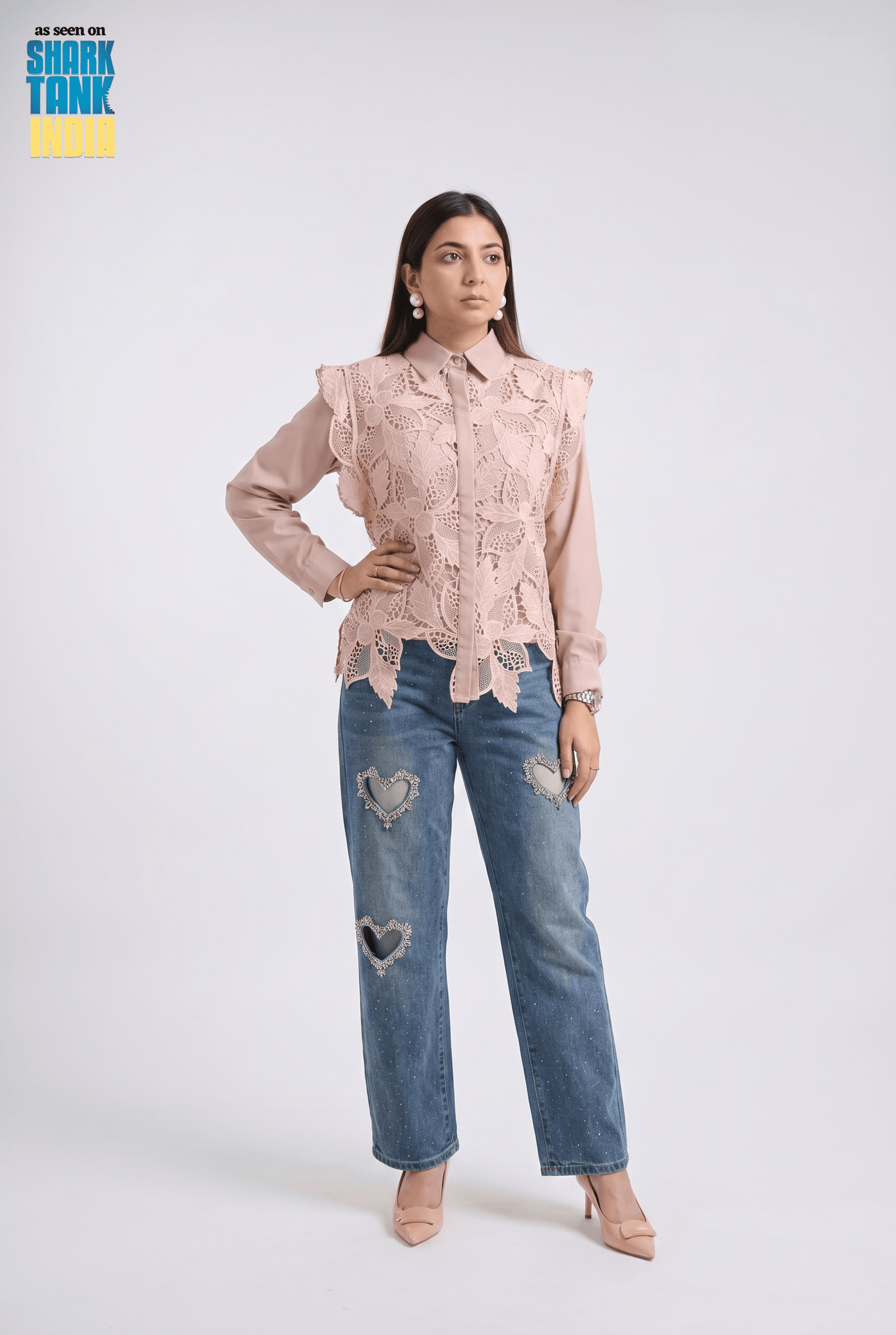 Woman wearing a pink lace blouse and blue jeans on a white background with 'Shark Tank' branding.