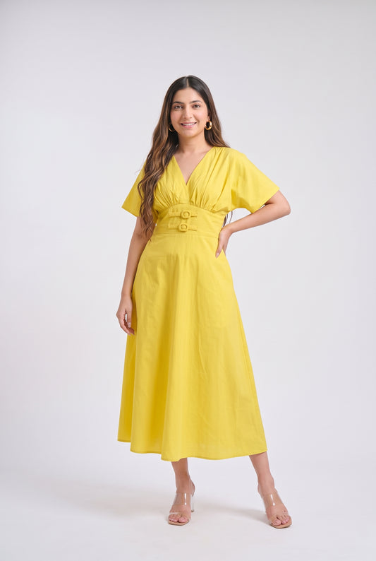 A woman modeling a bright yellow midi dress with short sleeves, a V-neckline, and a matching fabric belt with two gold-tone buttons, set against a plain light gray studio background.