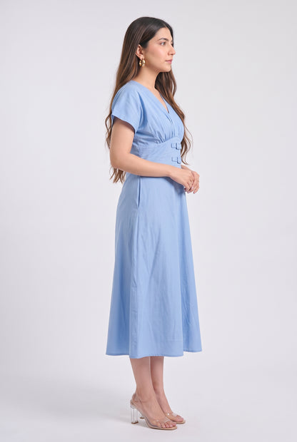 A woman modeling a light blue midi dress with short sleeves, a V-neckline, and a gathered waist, shown in profile against a plain light gray studio background.