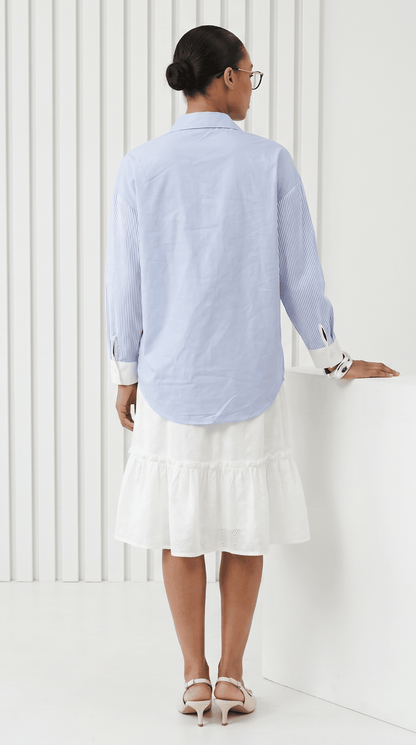 Woman wearing a light blue striped shirt and white skirt against a white background