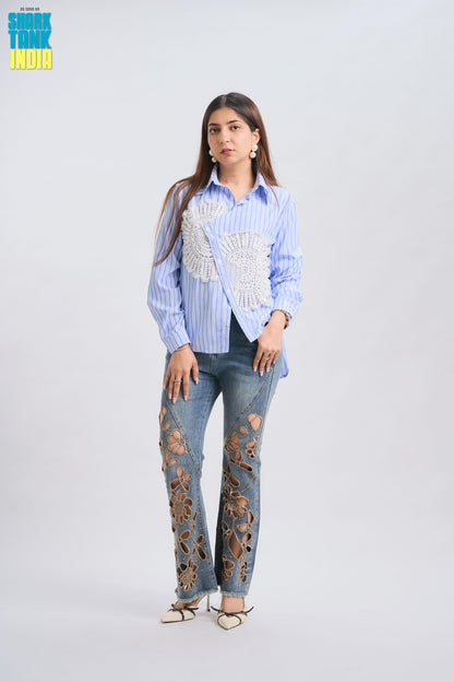 Woman wearing a blue striped shirt with decorative elements and distressed jeans on a white background