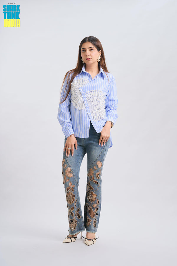 Woman wearing a blue striped shirt with decorative elements and distressed jeans on a white background