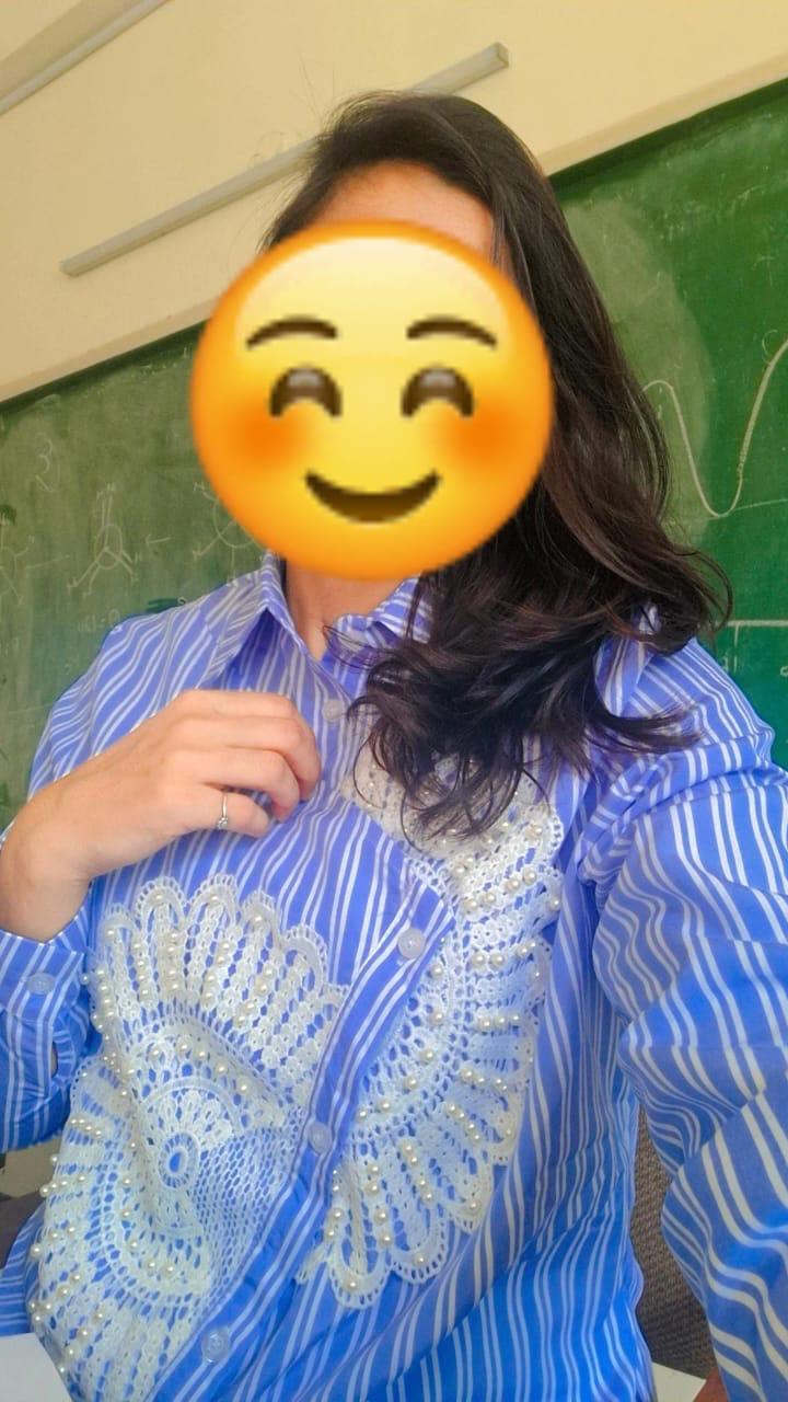 Person wearing a blue patterned shirt with a blurred face in front of a green chalkboard.