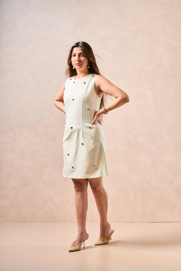 Woman wearing a white sleeveless dress with black buttons against a beige background