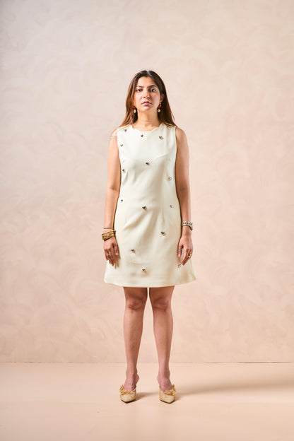 Woman wearing a cream dress with gold embellishments against a beige background