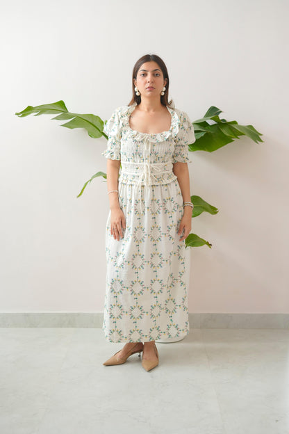 Woman wearing a floral dress standing against a white wall with green leaves.