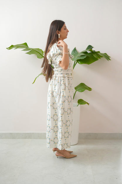 Woman in a floral dress standing next to a plant against a white wall