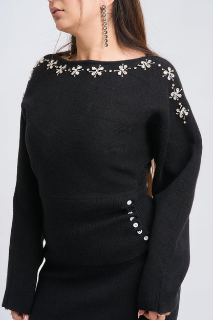 Black sweater with floral embellishments on a plain background