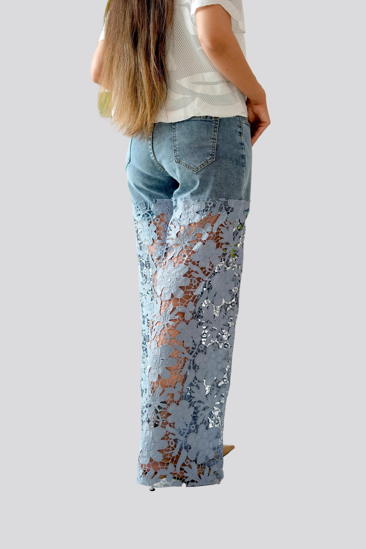 Person wearing a white shirt and blue jeans with floral pattern on a plain background