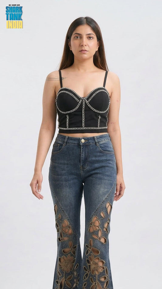 Woman wearing a black chain-embellished top and blue jeans with floral cutouts on a white background.