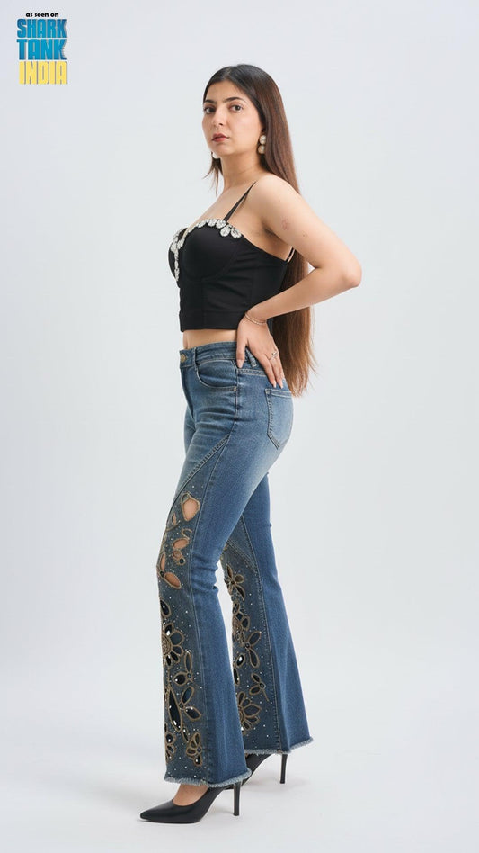 Woman wearing a black crop top and blue flared jeans with floral patterns on a white background